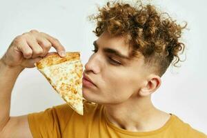 atraente homem dentro uma amarelo camiseta comendo pizza estilo de vida inalterado foto