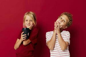 Garoto e menina descartável vidro com beber posando vermelho fundo foto