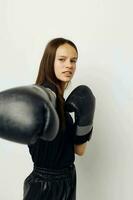 lindo menina dentro Preto Esportes uniforme boxe luvas posando ginástica Treinamento foto