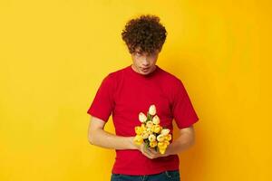 retrato do uma jovem encaracolado homem romântico posando com uma amarelo ramalhete do flores amarelo fundo inalterado foto