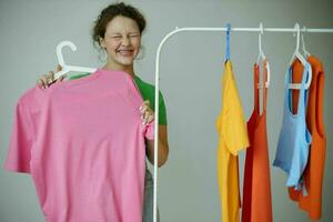 retrato do uma jovem mulher verde Camisetas perto roupas cabides isolado fundos inalterado foto