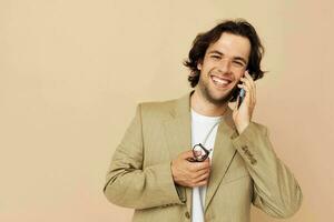alegre homem dentro uma terno posando emoções falando em a telefone bege fundo foto