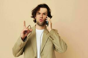 alegre homem dentro uma terno posando emoções falando em a telefone bege fundo foto