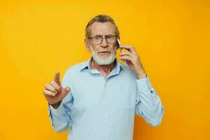 velho homem dentro uma azul camisa e óculos falando em a telefone amarelo fundo foto