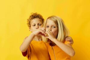 dois alegre crianças dentro amarelo Camisetas em pé lado de lado infância emoções amarelo fundo foto