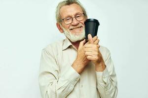 retrato do feliz Senior homem com uma cinzento barba dentro uma camisa e óculos luz fundo foto