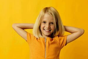 lindo pequeno menina sorrir mão gestos posando casual vestem Diversão amarelo fundo inalterado foto