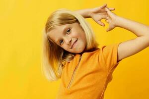 lindo pequeno menina sorrir mão gestos posando casual vestem Diversão amarelo fundo inalterado foto