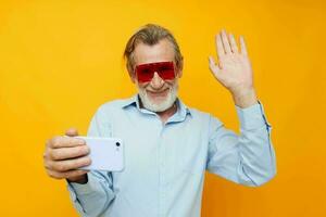 Senior grisalho homem azul camisas com óculos leva uma selfie cortada Visão foto