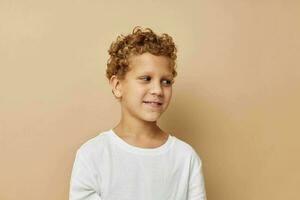 alegre Garoto com encaracolado cabelo dentro uma branco camiseta bege fundo foto