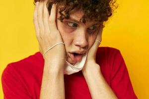 retrato do uma jovem encaracolado homem dentro uma vermelho camiseta médico mascarar proteção amarelo fundo inalterado foto