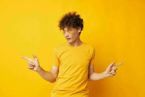 jovem cabelo encaracolado homem vestindo à moda óculos amarelo camiseta posando isolado fundo inalterado foto