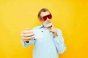 idosos homem dentro elegante vermelho óculos com uma telefone amarelo fundo foto