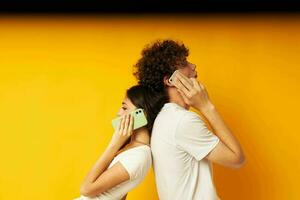 uma cara com uma menina dentro branco Camisetas falando em a telefone amarelo fundo foto