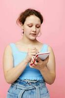adolescente menina escrevendo dentro uma vermelho caderno com uma caneta estude Rosa cor fundo inalterado foto