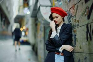 moda mulher retrato caminhando turista dentro à moda roupas com vermelho lábios caminhando baixa uma limitar cidade rua, viagem, cinematográfico cor, retro vintage estilo, dramático contra uma parede com grafite. foto