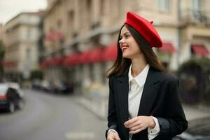 moda mulher sorrir com dentes em pé em a rua dentro frente do a cidade turista dentro à moda roupas com vermelho lábios e vermelho boina, viagem, cinematográfico cor, retro vintage estilo, urbano moda. foto