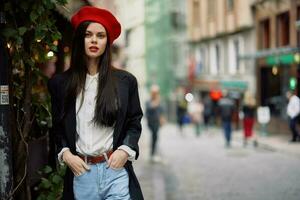 mulher moda modelo carrinhos em a rua dentro a cidade entre a multidão dentro uma Jaqueta e vermelho boina e jeans, cinematográfico francês moda estilo roupas, viagem para Istambul foto