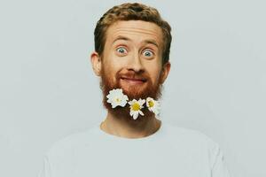 retrato do uma engraçado homem dentro uma branco camiseta com flores margaridas dentro dele barba em uma branco isolado fundo, cópia de lugar. feriado conceito e Parabéns. foto