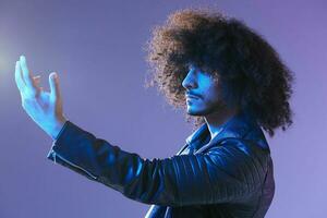 retrato do moda homem com encaracolado cabelo em azul fundo multinacional, colori luz, Preto couro Jaqueta tendência, moderno conceito. foto