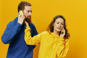 mulher e homem alegre casal com telefones dentro mão falando em célula telefone torto sorrir alegre, em amarelo fundo. a conceito do real família relacionamentos, falando em a telefone, trabalhos on-line. foto