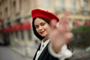 moda mulher sorrir com dentes em pé em a rua dentro frente do a cidade turista Segue mim à moda roupas com vermelho lábios e vermelho boina, viagem, cinematográfico cor, retro vintage estilo, urbano moda. foto