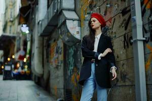 moda mulher retrato caminhando turista dentro à moda roupas com vermelho lábios caminhando baixa uma limitar cidade rua, viagem, cinematográfico cor, retro vintage estilo, dramático contra uma parede com grafite. foto