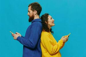 mulher e homem alegre casal com telefones dentro seus mãos torto sorrir alegre, em azul fundo. a conceito do real família relacionamentos, falando em a telefone, trabalhos on-line. foto