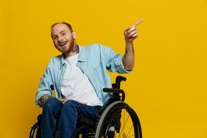 uma homem dentro uma cadeira de rodas problemas com a musculoesquelético sistema parece às a Câmera mostra uma dedo sobre, com tatuagens em dele mãos senta em uma amarelo estúdio fundo, saúde conceito homem com deficiências foto