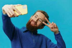 retrato do uma homem com uma telefone dentro dele mãos blogueiro leva selfies, em uma azul fundo. comunicando conectados social meios de comunicação, estilo de vida foto