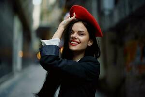 moda mulher sorrir com dentes e Diversão turista dentro à moda roupas dentro Jaqueta e vermelho boina caminhando baixa limitar cidade rua vôo cabelo, viagem, francês estilo, cinematográfico cor, retro vintage estilo. foto