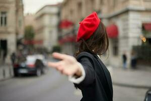 moda mulher sorrir com dentes em pé em a rua dentro frente do a cidade turista Segue mim à moda roupas com vermelho lábios e vermelho boina, viagem, cinematográfico cor, retro vintage estilo, urbano moda. foto