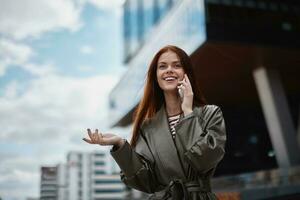 mulher o negócio falando em a telefone e sorridente com dentes contra a pano de fundo do cidade edifícios, tecnologia e o negócio desenvolvimento conceito conectados foto