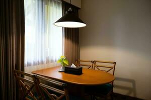 Sombrio casa interior com madeira jantar mesa aceso de lâmpada, tarde luz para jantar. foto