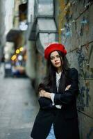 moda mulher retrato caminhando turista dentro à moda roupas com vermelho lábios caminhando baixa uma limitar cidade rua, viagem, cinematográfico cor, retro vintage estilo, dramático contra uma parede com grafite. foto