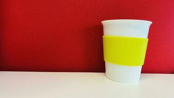 uma branco papel copo com uma amarelo fronteira em uma branco mesa. fundo vermelho muro. foto