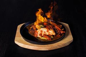 fajitos, carne em uma frigideira com fogo em uma bandeja de madeira, bela porção, fundo escuro foto