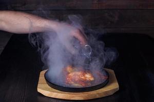 fajitos, carne em uma frigideira com fogo em uma bandeja de madeira, bela porção, fundo escuro foto