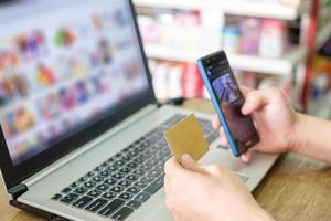 mão segurando o cartão de crédito e usando laptop com smartphone para compras de pagamento online foto