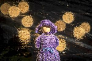 boneca de madeira com vestido azul de crochê contra um fundo desfocado com luzes brilhantes