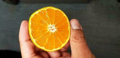 fechar acima mão e dedo segurando fresco metade fatia do laranja com borrado cinzento ou cinzento chão fundo. saudável Comida e fruta conceito. foto