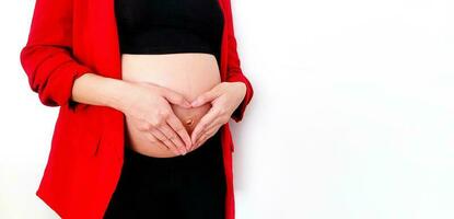 fechar acima grávida mulher dentro vermelho terno formando uma formato de coração com dela mãos sobre dela estômago ou barriga isolado em branco fundo e cópia de espaço com recorte caminho. gravidez 7-9 meses, maternidade foto