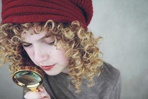 closeup retrato de uma bela e jovem mulher engraçada com olhos azuis e cabelo loiro encaracolado investigando com uma lupa foto