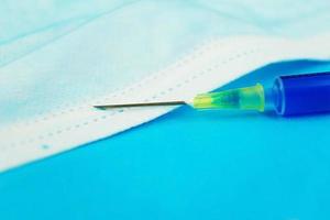 uma macro detalhada de uma seringa com agulha em uma máscara médica com fundo azul foto