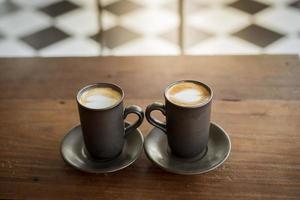 latte art quente com vidro preto na mesa de madeira foto