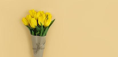 buquê de tulipas amarelas embrulhadas em papel ofício em fundo bege com copyspace. foto