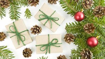 cartão postal de férias com caixas de presente de artesanato, galhos de árvores de abeto, cones e enfeites de Natal vermelhos em um fundo branco. foto