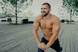 desportivo do homem manhã rotina alongamento, posando, ao ar livre dar certo. alegre expressão, barba por fazer, nu tronco. foto