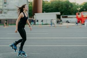 patins enérgico magro jovem sorridente na estrada da cidade gosta de passar o tempo livre ativamente se move rapidamente tem cabelos escuros flutuando no vento leva um estilo de vida saudável. fins de semana ativos. foto ao ar livre