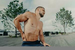 com a barba por fazer desportista mais baixo costas dor depois de treinamento. ao ar livre poses. exercício ferida. Atlético cara necessidades massagem. foto